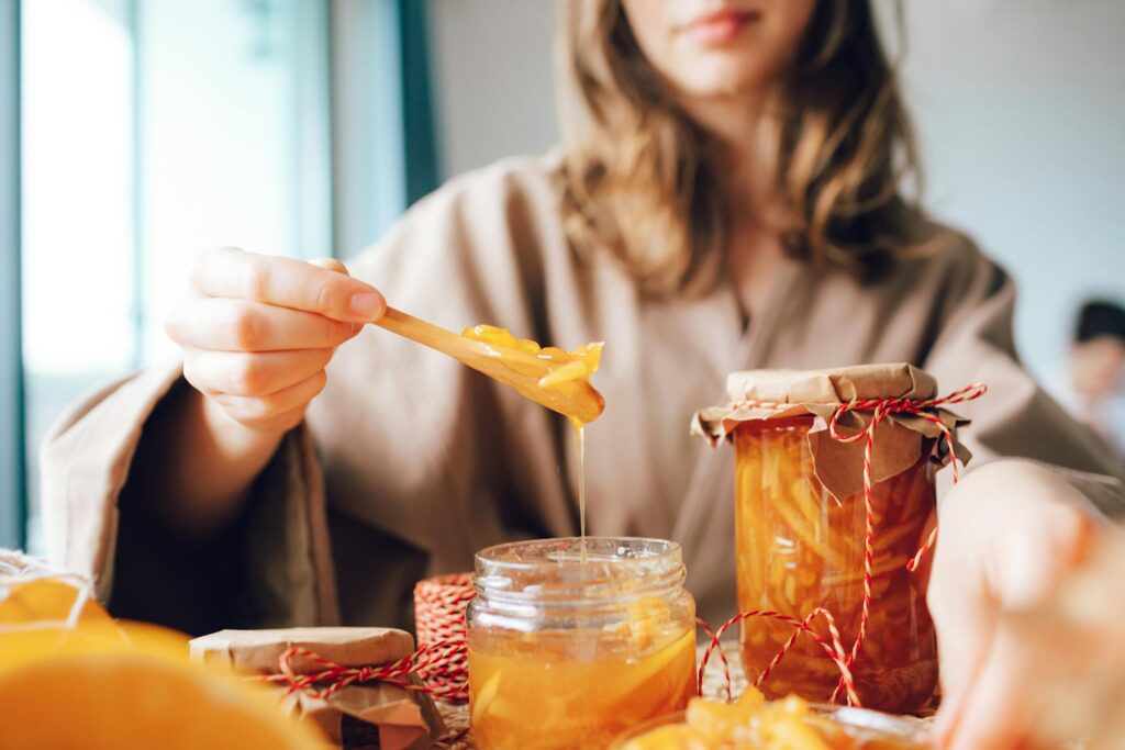 Close-up of a woman preparing fresh orange marmalade in glass jars, capturing the essence of homemade cuisine.
