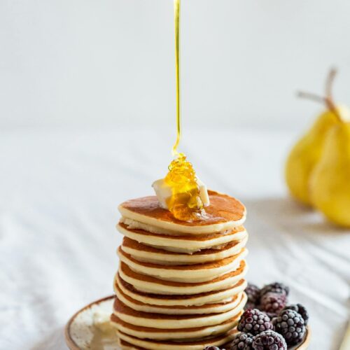 Mouthwatering stack of pancakes drizzled with honey, garnished with blackberries.