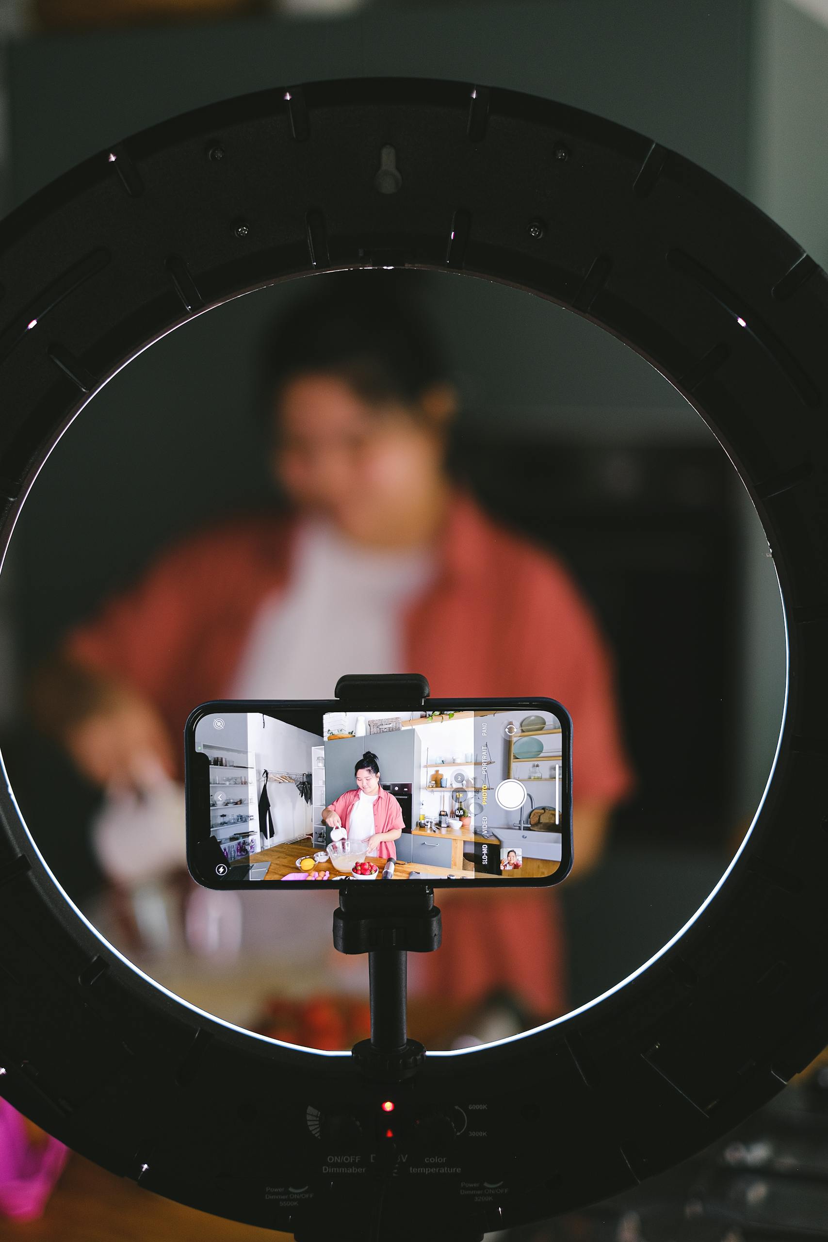 Woman demonstrating a cooking tutorial on camera, surrounded by kitchen equipment and lighting setup.