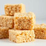 A close-up image of stacked Rice Krispies Treat squares, showcasing their gooey texture and golden color against a neutral background.